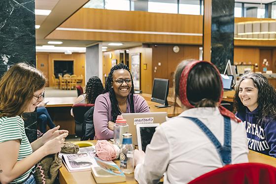 图为一群波胆网站的学生坐在珍妮·金·梅隆图书馆的学习桌旁，微笑着一起学习. 